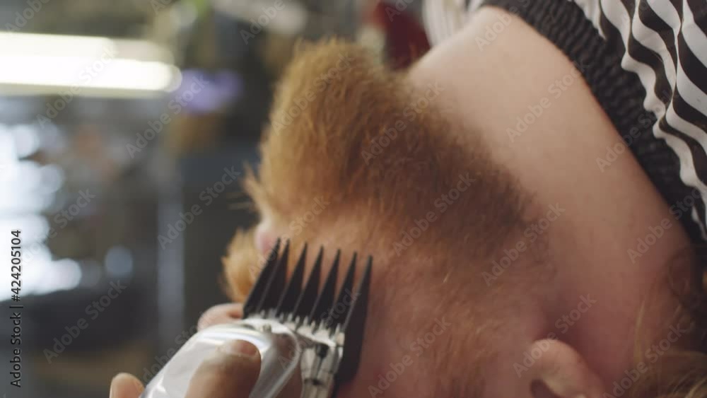 Vertical close up shot of Caucasian man leaning back and getting his beard trimmed with hair clippers by barber Vertical close up shot of Caucasian man leaning back and getting his beard trimmed with hair clippers by barber