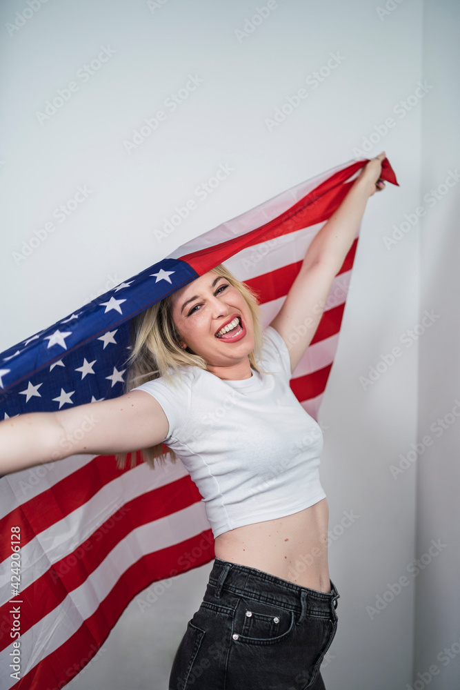 Fototapeta premium Chica guapa rubia con bandera americana feliz celebrando 4 de julio