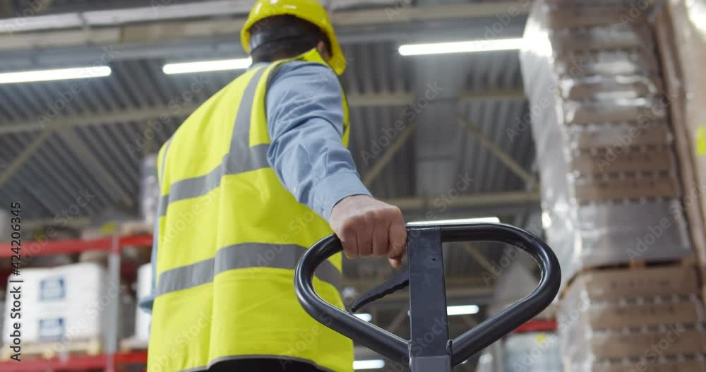 Senior worker in warehouse using hand pallet stacker to transport goods.