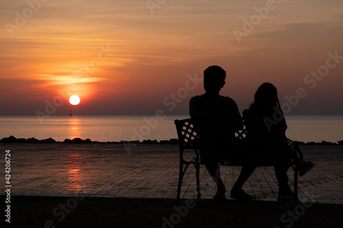 silhouette couple sitting on the bench in the morning and sunrise behind them