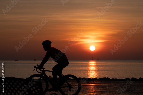 silhouette man cycling in the morning and sunrise behind them © Pijitra