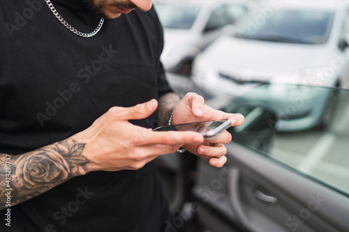 Hands with tattoos holding a phone near the car