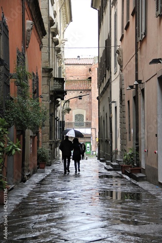 A well-dressed male female couple holding an umbrella walking down a wet lane, paved with large stone slabs, in the historic center of Pistoia, Italy, on a rainy early spring day © Peter
