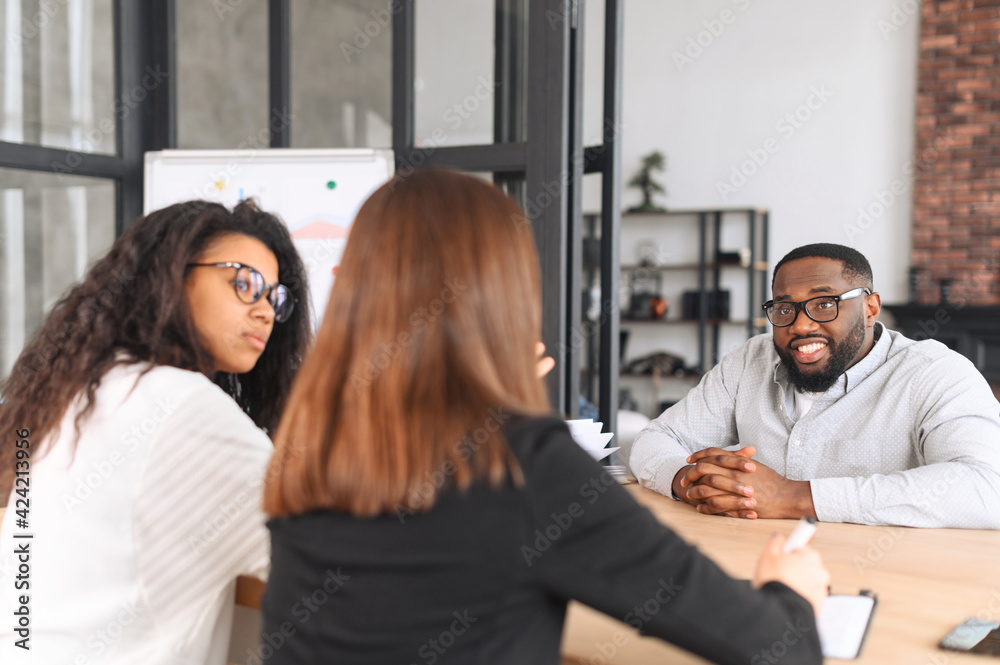 The working process at contemporary coworking. Diverse team of young ambitious people brainstorming together, an African-American male in eyeglasses listening carefully his female colleague