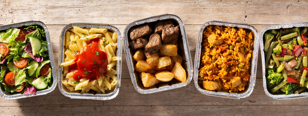 Take away healthy food in foil boxes on wooden table. Panorama view