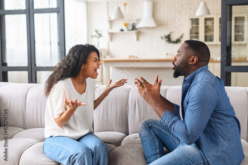 Multiracial couple is arguing at home. Angry young spouses screaming and misunderstanding to each other, African-American couple has relationships problem photo