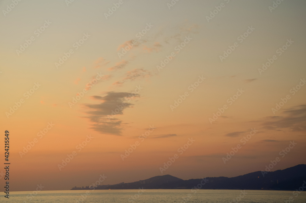Evening orange sky with clouds, sea and mountains