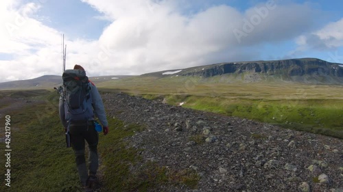 Male hiker walking in Saltoluokta, Northern Sweden. Snow on mountain and green grass in the background. photo