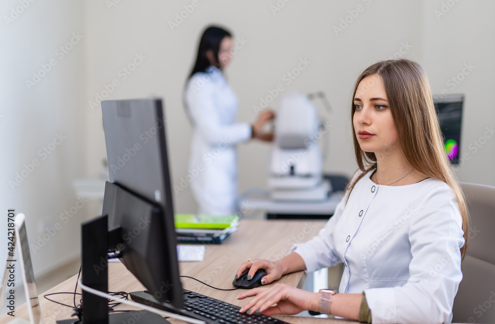 Doctor is working at computer in clinic office. Medic in white scrubs is sitting at table. Modern interior in hospital. Doctor is working at computer in clinic office. Medic in white scrubs is sitting at table. Modern interior in hospital.