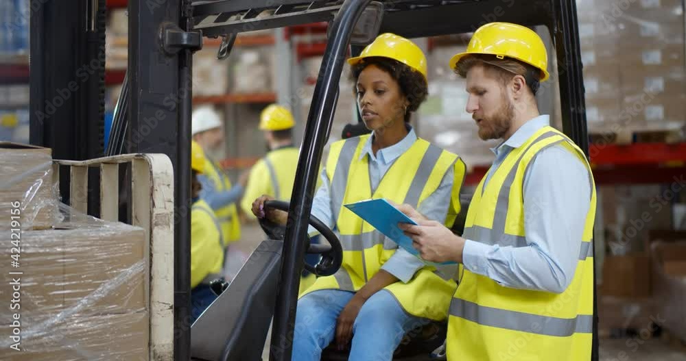 African female fork lift truck driver discussing checklist with foreman in warehouse African female fork lift truck driver discussing checklist with foreman in warehouse