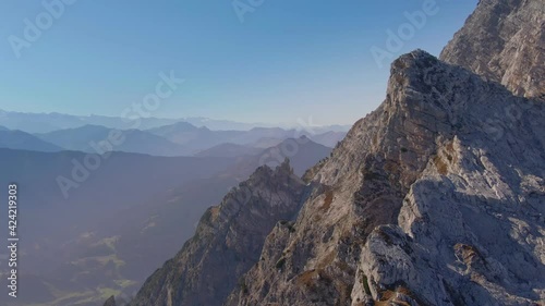 An aerial drone shot of a steep rocky mountain side with hazy rolling mountains in the distance. photo