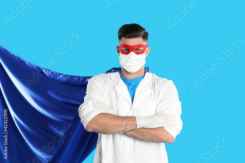 Doctor wearing face mask and cape on light blue background. Super hero power for medicine photo