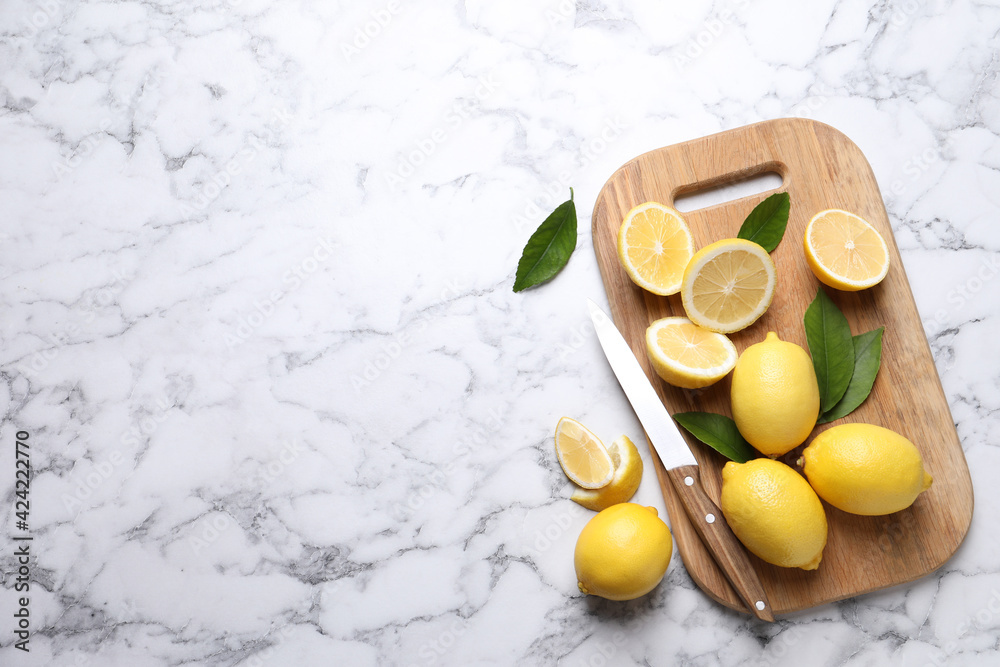 Many fresh ripe lemons with green leaves and knife on white marble table, flat lay. Space for text Many fresh ripe lemons with green leaves and knife on white marble table, flat lay. Space for text