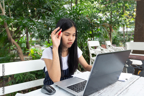 Asian women is thinking task with laptop. she sitting in the park on white table.