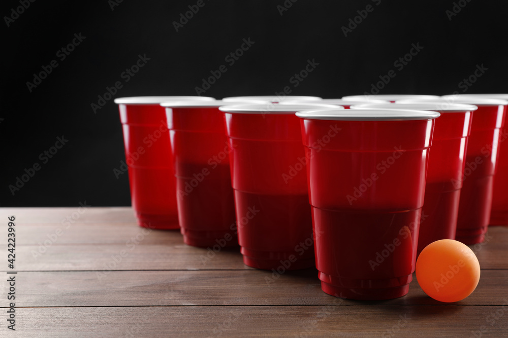 Plastic cups and ball for beer pong on wooden table against black  background Stock-Foto | Adobe Stock