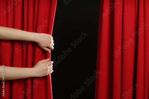 Woman opening red front curtains on black background, closeup