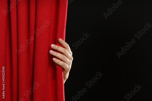 Woman opening red front curtains on black background, closeup. Space for text