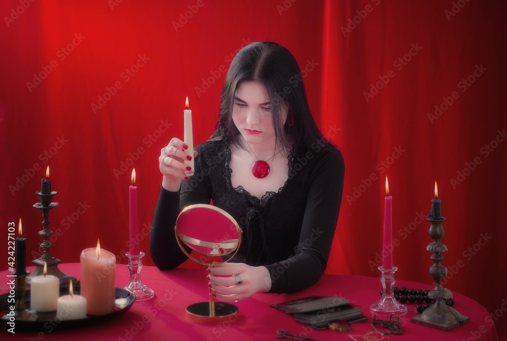 young girl in  black dress is wondering in front of mirror on  red background