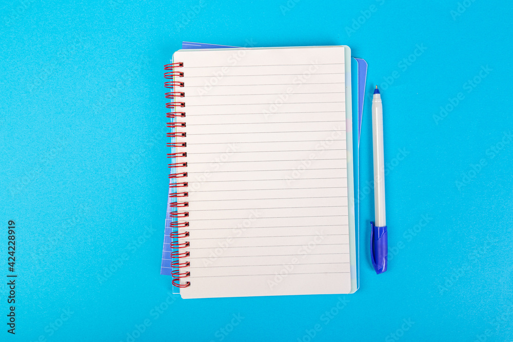 stack of school exercise books on blue background, spiral notepad with blank page and pen on table top view stack of school exercise books on blue background, spiral notepad with blank page and pen on table top view