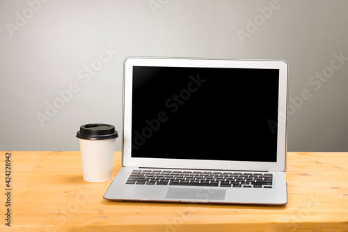 Mockup blank laptop screen with coffee on wooden table in coworking space.