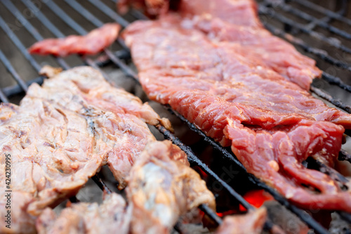 Фотография A view of cuts of beef sirloin flap cooking on a kettle grill.