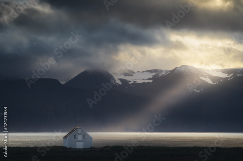 House on the coast in Northeast Iceland. Sun ray through the clouds from the sky. Mountains nature landscape at sunset