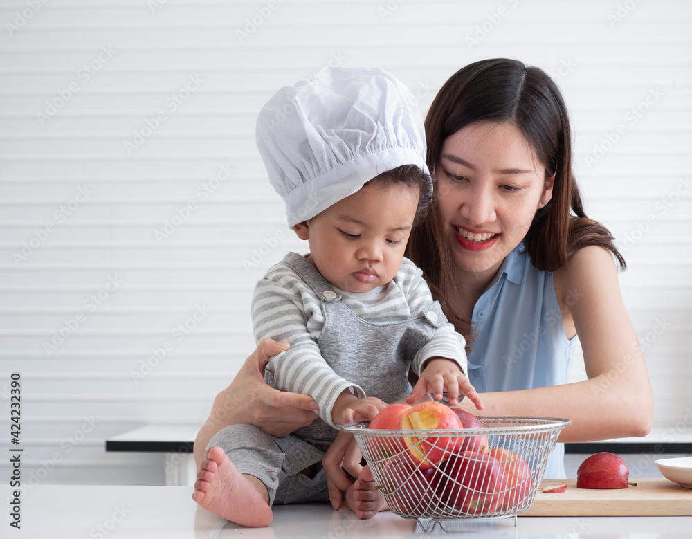 Happy young Asian mother Embrace her adorable little son while select red apples at home in the kitchen. Funny educational for children concept.. Happy young Asian mother Embrace her adorable little son while select red apples at home in the kitchen. Funny educational for children concept..
