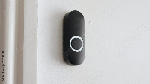 Apartment door bell being pressed. A woman presses a black doorbell with her finger on a white wall. photo