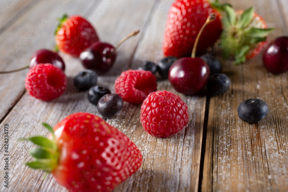 A view of several varieties of fruit and berries scattered on a wooden table surface, featuring strawberry, blueberry, raspberry and cherry. A view of several varieties of fruit and berries scattered on a wooden table surface, featuring strawberry, blueberry, raspberry and cherry.