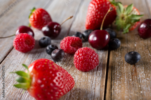 A view of several varieties of fruit and berries scattered on a wooden table surface  featuring strawberry  blueberry  raspberry and cherry.