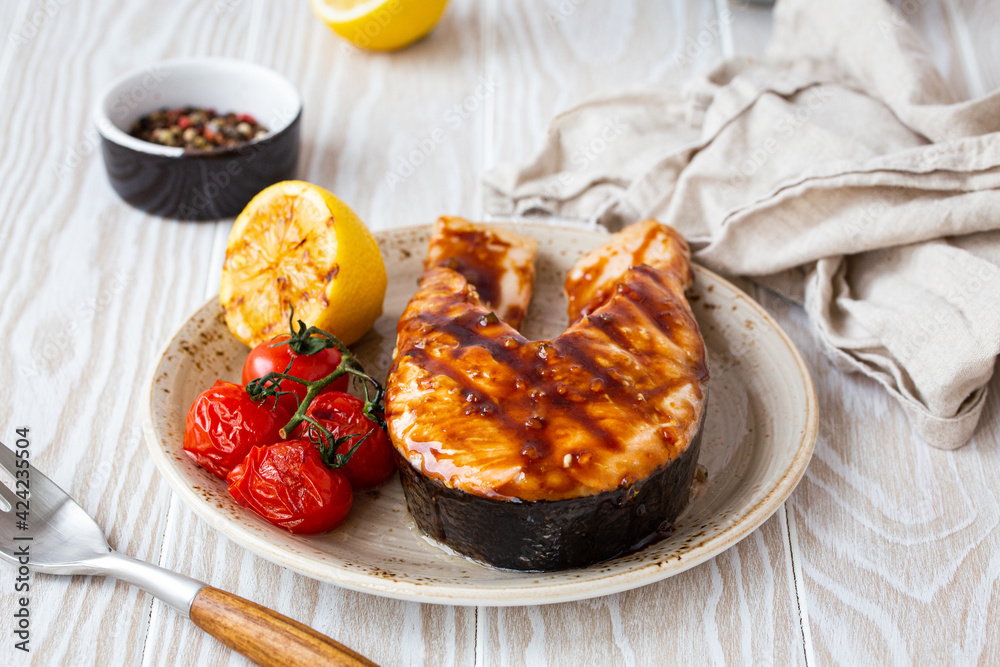 Grilled salmon steak glazed with teriyaki sauce, vegetables and lemon served on ceramic plate on rustic white wooden table from angle view, selective focus 