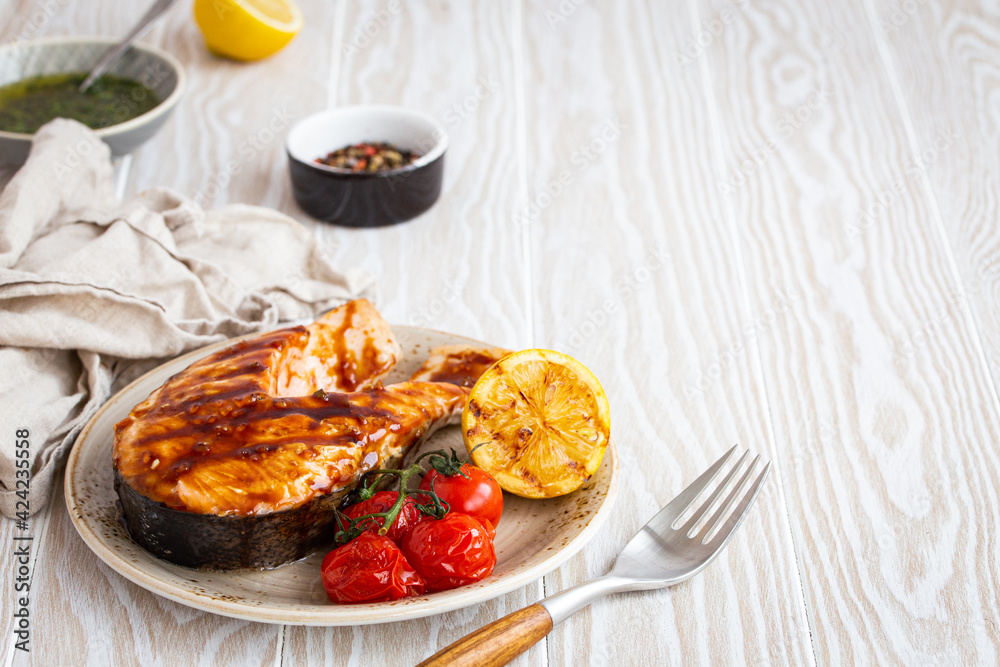 Grilled salmon steak glazed with teriyaki sauce, vegetables and lemon served on ceramic plate on rustic white wooden table from angle view, selective focus with space for text