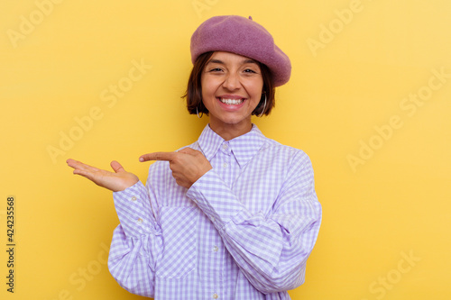 Young mixed race woman wearing a beret isolated on yellow background excited holding a copy space on palm.