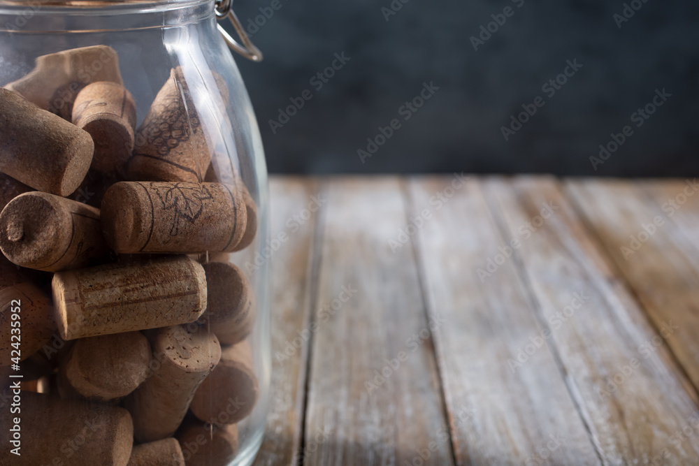 A view of a jar of wine corks, sitting on the left side of the frame, on a wooden table surface. A view of a jar of wine corks, sitting on the left side of the frame, on a wooden table surface.