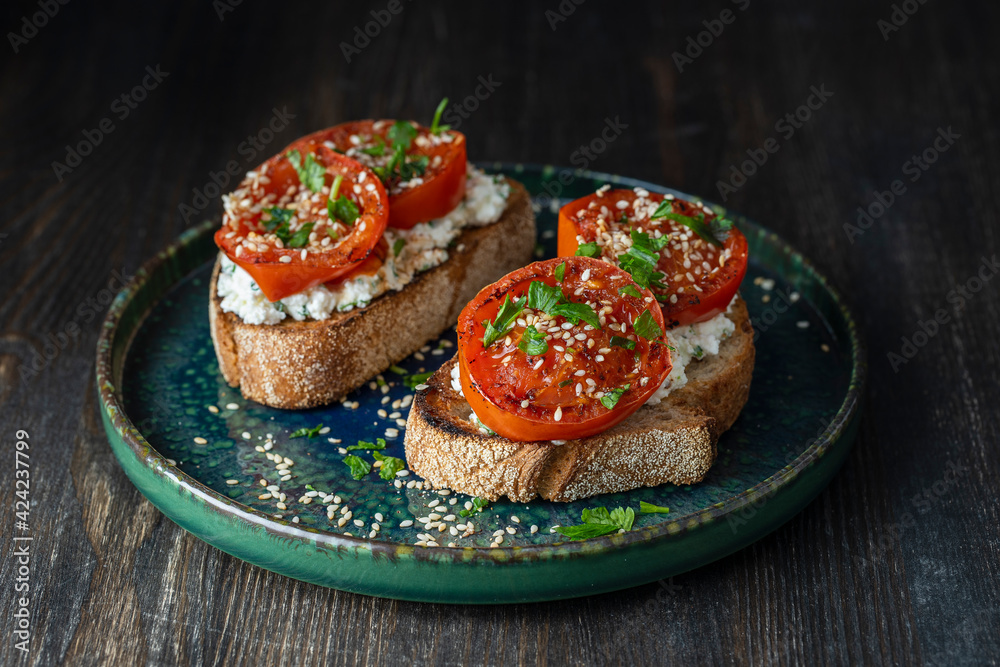 Delicious toasted bread with roasted red tomatoes, feta cheese, sesame seeds and herbs on plate