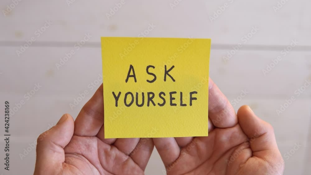 ASK YOURSELF written on a yellow sticker. Man hands holding a yellow sticky note paper on a white background