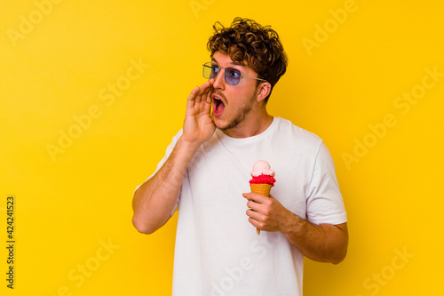 Young caucasian man eating an ice cream isolated on yellow background shouting and holding palm near opened mouth.