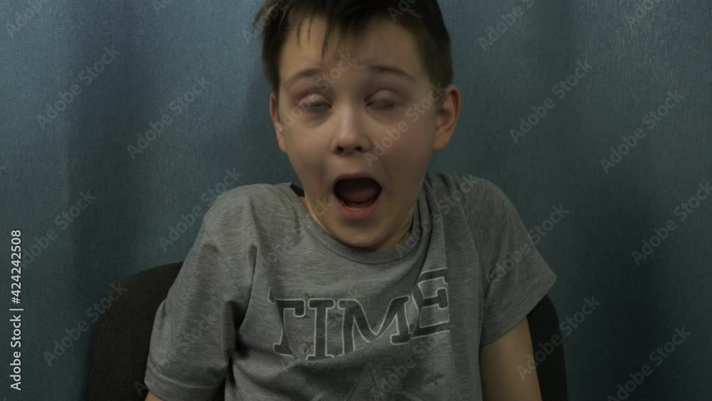 the boy yawns sitting on a chair. blinking his eyes, trying to wake up