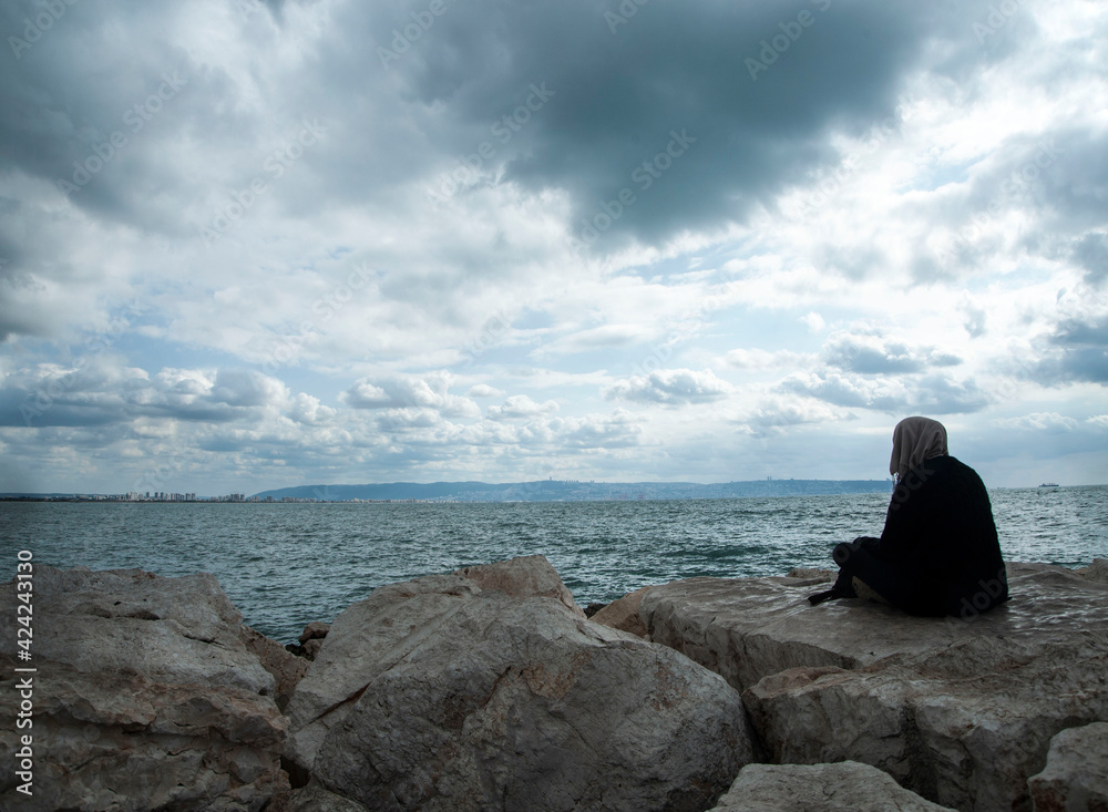 Lonely woman in black clothes sits near the sea.