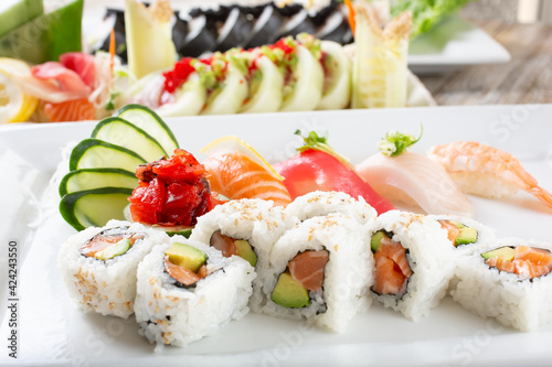 A view of a plate with salmon avocado roll slices and a variety of nigiri, with more sushi rolls in the background.