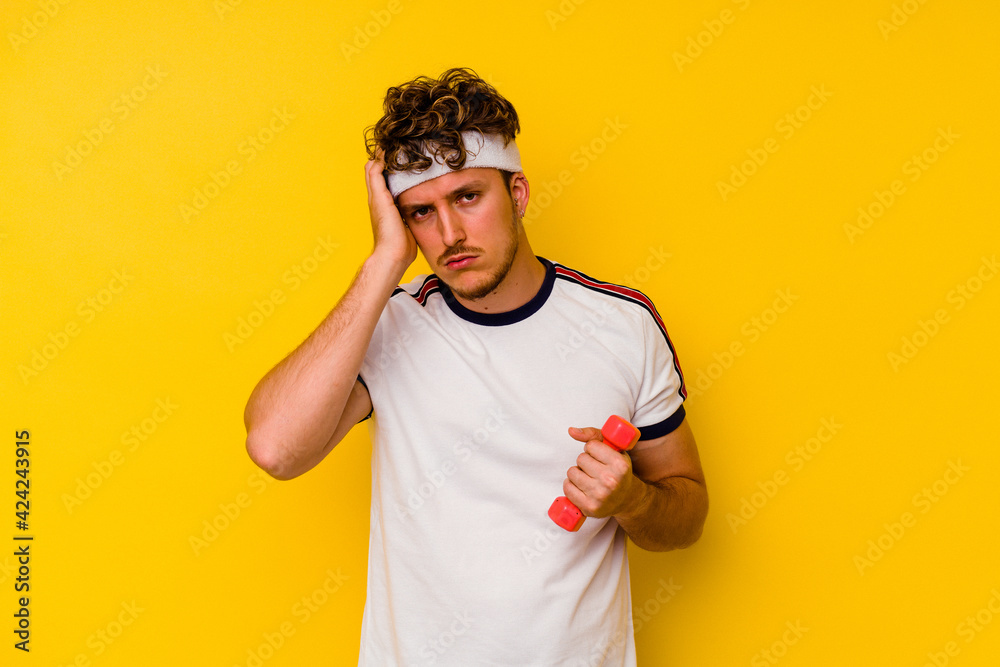 Young sport caucasian man holding a dumbbell isolated on a yellow background being shocked, she has remembered important meeting. Young sport caucasian man holding a dumbbell isolated on a yellow background being shocked, she has remembered important meeting.