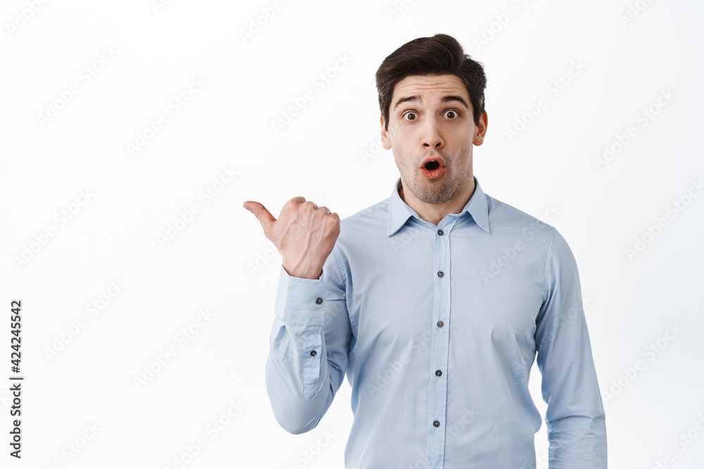 Wow look. Impressed ceo corporate man in office clothing, gasping amazed, pointing aside at promo text, show logo, standing surprised against white background Wow look. Impressed ceo corporate man in office clothing, gasping amazed, pointing aside at promo text, show logo, standing surprised against white background