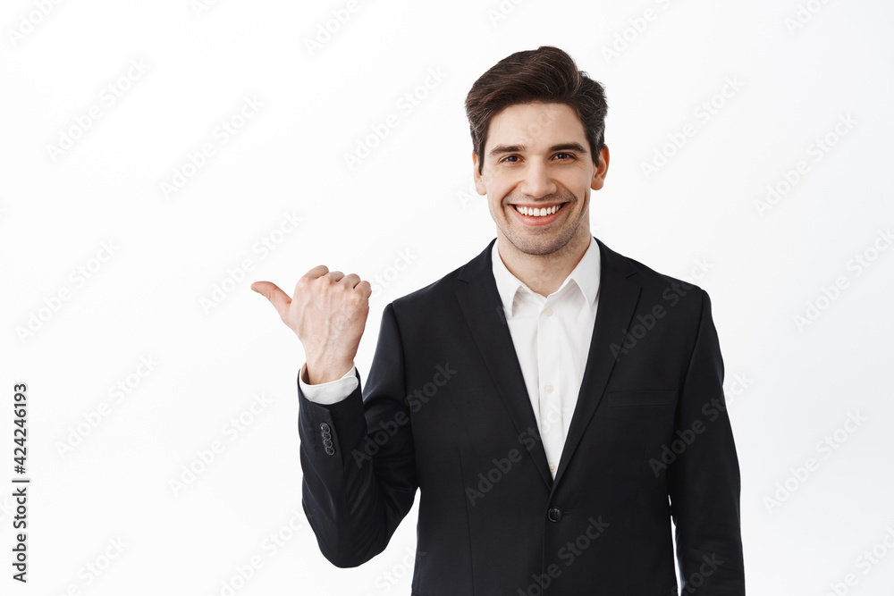 Smiling businessman, corporate man in suit pointing aside and showing advertisement on copyspace, wearing business suit, standing over white background Smiling businessman, corporate man in suit pointing aside and showing advertisement on copyspace, wearing business suit, standing over white background