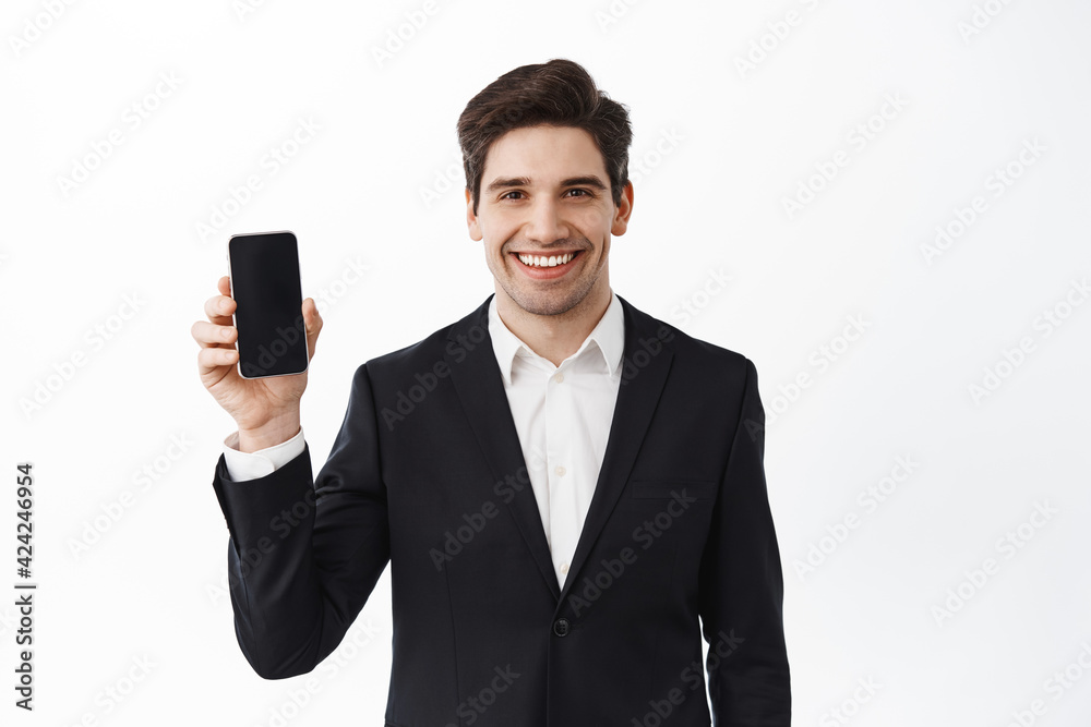 Confident businessman in black suit showing empty smartphone screen, smiling, introduce an application, online store or promo, white background Confident businessman in black suit showing empty smartphone screen, smiling, introduce an application, online store or promo, white background