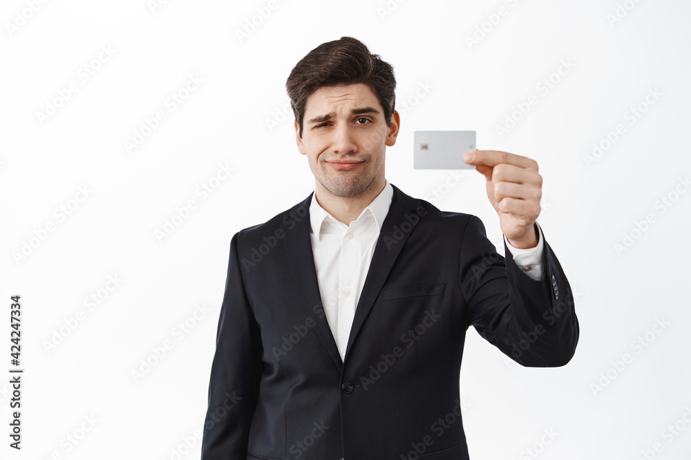 Skeptical, displeased male entrepreneur, business man shows credit card and frowning upset, dislike bank, standing over white background Skeptical, displeased male entrepreneur, business man shows credit card and frowning upset, dislike bank, standing over white background