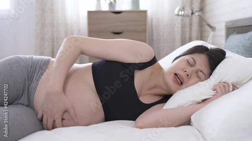 Asian expectant woman awake by contraction pain and grasping pillow is going to labor in the morning at home.