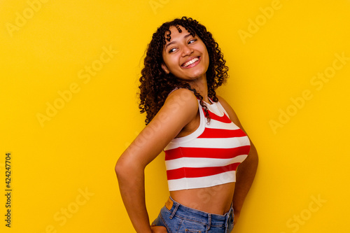 Young mixed race woman isolated on yellow background laughs happily and has fun keeping hands on stomach.