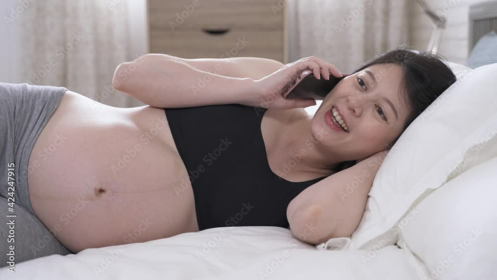 portrait asian female in her confinement during pregnancy is receiving call from family, and talking on phone while resting in the bedroom. portrait asian female in her confinement during pregnancy is receiving call from family, and talking on phone while resting in the bedroom.