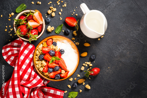 Greek yogurt granola with fresh berries on black stone table.