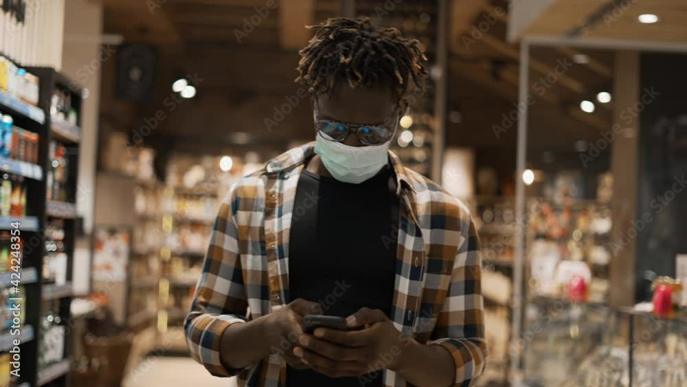 African American man in mask busy with smartphone walks at the store African American man in mask busy with smartphone walks at the store